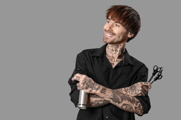 Young tattooed barber with hair spray and scissors on grey background