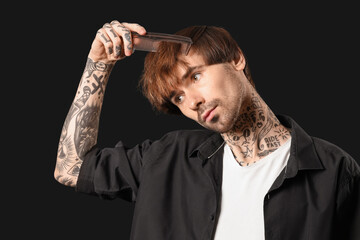 Young tattooed barber combing hair on dark background, closeup