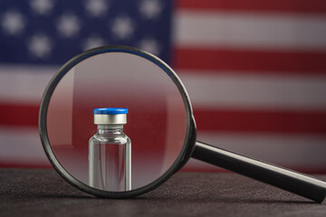 Vaccine vial and magnifying glass on US flag background.