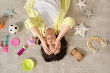 Tired young mother resting among scattered children's toys in living room