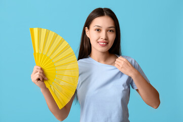 Smiling young woman with hand fan on blue background