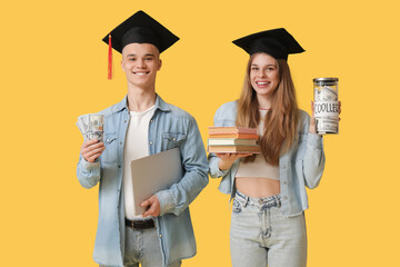 Young students in graduation hats with jar bank, money and laptop on yellow background. Concept of...