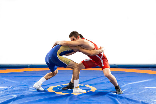 Two  strong men in blue and red wrestling tights are wrestling  on a white background. Wrestlers doing grapple.
