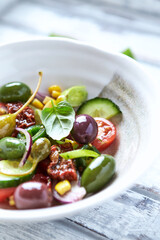 Simple Salad with Green and Kalamata Olives, Cucumber, Cherry and marinated Tomatoes, Capers and Jalapeno Pepper. Bright wooden background.