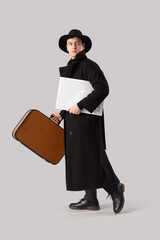 Male spy with newspaper and bag walking on light background