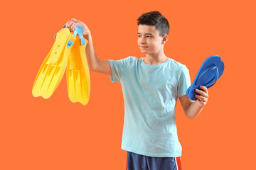 Cute little happy boy with flippers and flip flops on orange background