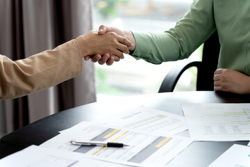 businesswomen sits and shakes hands to greet or congratulate a work desk full of documents
