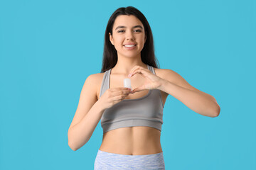 Happy smiling young woman holding crystal deodorant and making heart with her hand on blue...