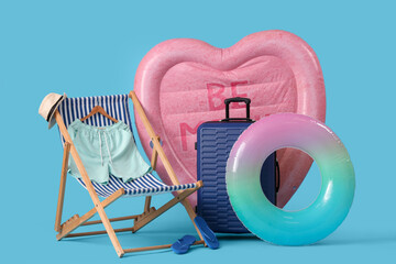Swimming mattress in shape of heart, inflatable ring and suitcase on blue background