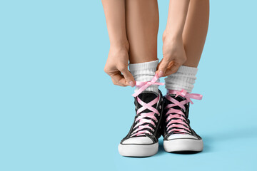 Young woman in sneakers with pink bows on blue background, closeup