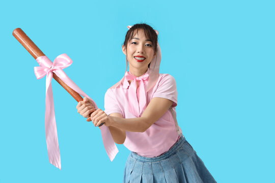Young Asian woman with pink bows and bat on blue background