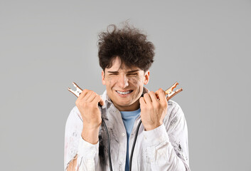 Electrocuted young man with burnt face and jumper cables on light background