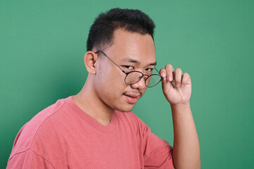 Portrait of Asian man looking at camera while holding his eyeglasses isolated on green background