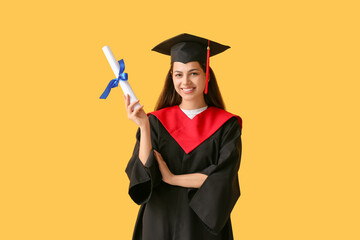 Happy female graduate with diploma on yellow background