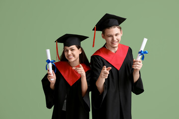 Happy graduate couple with diplomas pointing at viewer on green background