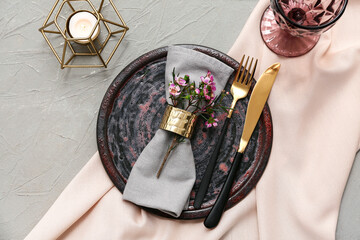 Table setting with beautiful flowers and burning candle on grey background