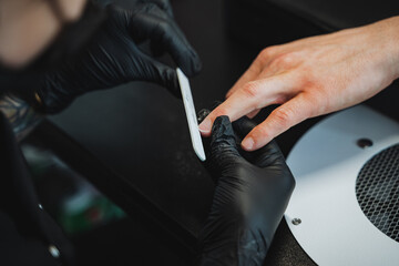 The womans nails are being expertly painted by a tech in black gloves