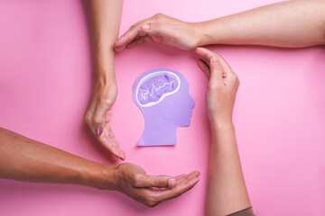 World Mental Health Day.  Diverse hands protect encephalography brain paper cutout. Autism,...