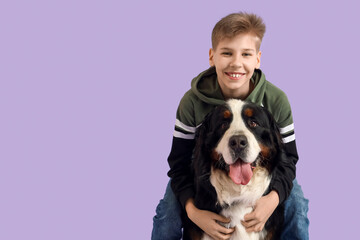 Little boy hugging Bernese mountain dog on lilac background
