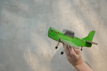 kid hand with green antique aircraft on grey wall background.