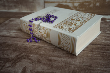 Rosary and bible on wooden background.