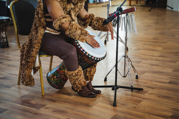 Person seated on hardwood chair drumming with leg on membranophone