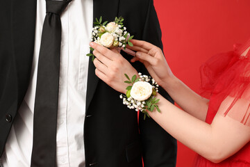 Beautiful girl pinning boutonniere her prom date on red background