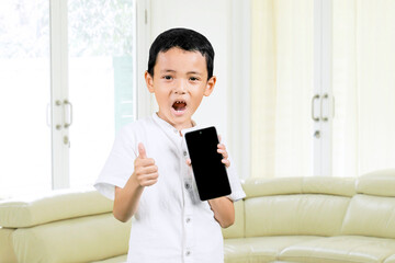 Cute child showing thumb up while holding a blank mobile phone