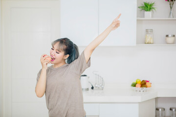 Asian woman singing with a wooden spatula while cooking in the kitchen at home