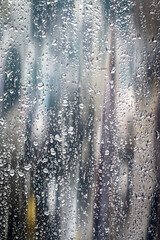 window glass surface with raindrops against gray blurred urban background.