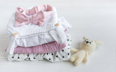 Stack of baby clothes, pink headband and knitted toy bunny.