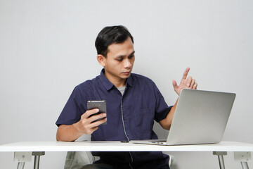 joyfull happy asian man holding mobile phone while sitting in front of laptop computer. on isolated background