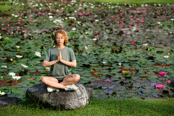 A young girl, with blond curly hair, folds her hands in namaste, meditates, sitting on a large...