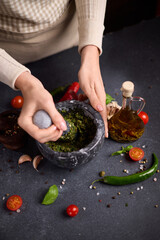 woman pounding in a stone marble mortar green sauce chopped ingredients - capers, fennel and basil