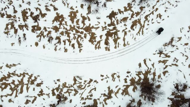 Aerial top down view of an ATV drifting around a corner on a frozen river trail.