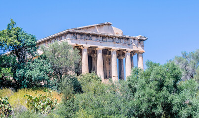The famous Hephaistos temple surrounded by green trees under a blue sky, in Athens, Greece.
