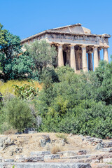 The famous Hephaistos temple surrounded by green trees under a blue sky, in Athens, Greece.