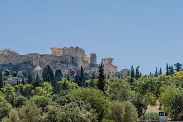 View of the Acropolis with historic ruins and greenery against a clear sky, in Athens, Greece