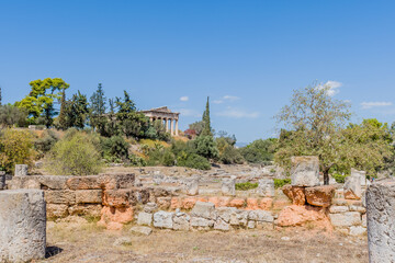 Greek archaeological site with wild vegetation and a distant view of Hephaistos temple against blue sky, in Athens, Greece