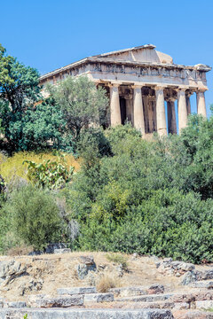 The famous Hephaistos temple surrounded by green trees under a blue sky, in Athens, Greece.