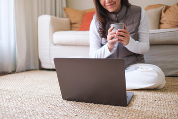 Closeup image of a young woman drinking coffee while working on laptop computer at home - 785918908