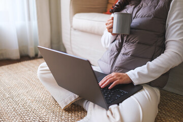 Closeup image of a woman drinking coffee while working on laptop computer at home - 785918970