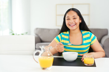Obraz na płótnie Canvas Portrait, happy girl and smile in home with breakfast, juice and excited for healthy diet in morning. Nutrition, growth and development, hungry child at table with cereal and drink at start of day