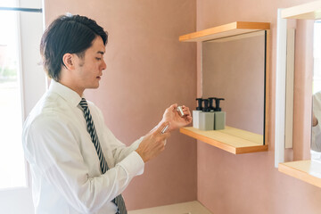 朝出勤前に手首に香水をつけるスーツ姿の若いアジア人ビジネスマン（メンズコロン・メンズ香水）
