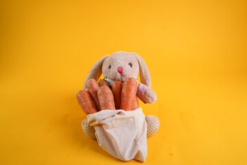 A brown toy rabbit on a yellow background with a large carrot