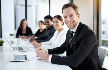 Meeting, portrait and happy man with business people in conference room with confidence, tech or plan. Boardroom, men and women in corporate workshop with laptop, report and smile at startup office