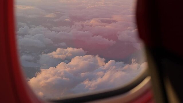 The airplane window offers a scenic vista of sunlit clouds, casting a serene glow, symbolizing the essence of travel and vacation.