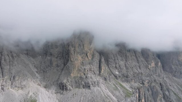 Aerial drone footage captures the rugged peaks of Passo Gardena enveloped in clouds as the drone ascends and turns to the right. Filmed in the Dolomites, Trentino, South Tyrol, Italy. LuPa Creative.