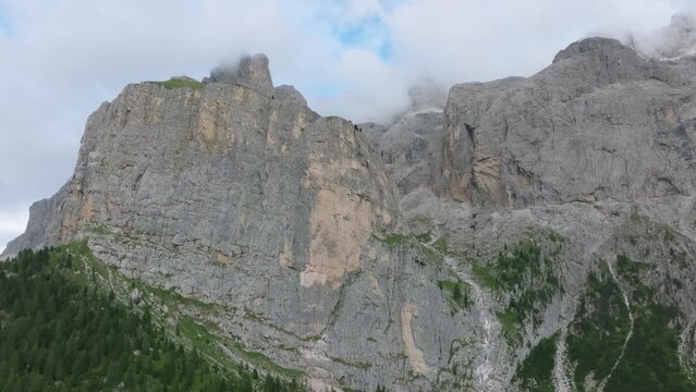 Cinematic aerial footage of a drone ascending  towards the Selva rugged mountain range near Passo Gardena, Dolomites.The drone flies forward, revealing the mountains covered in clouds. LuPa Creative.