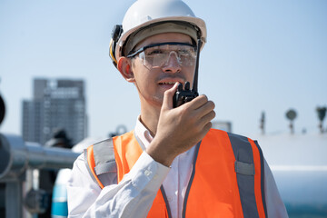Portrait Asia male engineer in protective workwear is performing a conducts system check with use walkie talkie at rooftop building	